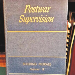 May include: A vintage book titled "Postwar Supervision" with gold lettering on a blue cover. The book also has the text "Building Morale" and "Conference 9". The book is part of a collection of books.