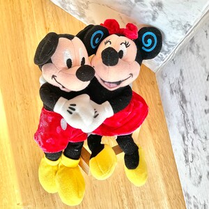 Mickey Minnie Mouse Hugging plushie doll, holding hands, blue swirls  on ears, smiling, above view.