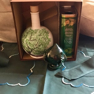 May include: A brown cardboard box with a green ceramic bottle with a tree design, a green ceramic bottle stopper, and a can of olive oil. The can has the text "De consumeren" and "Contenuto 1/2 l" printed on it.