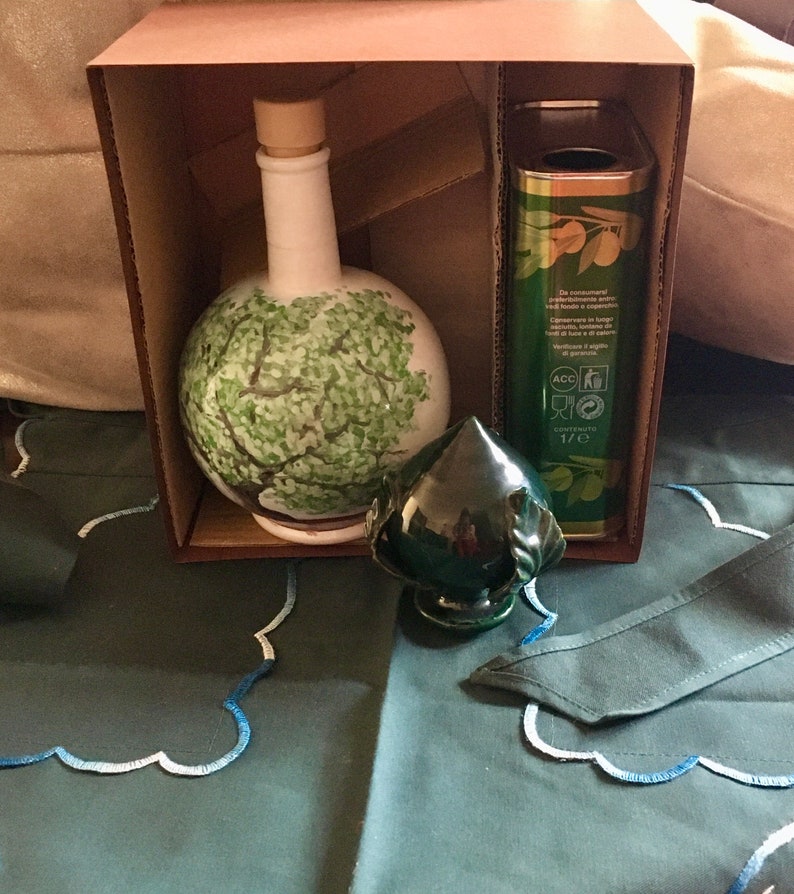 May include: A brown cardboard box with a green ceramic bottle with a tree design, a green ceramic bottle stopper, and a can of olive oil. The can has the text "De consumeren" and "Contenuto 1/2 l" printed on it.