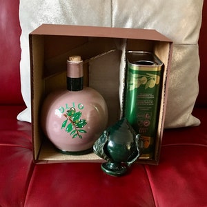 May include: A brown cardboard box with a green ceramic olive oil bottle, a green ceramic olive branch bottle stopper, and a can of olive oil. The can has the text "Olio Extra Vergine di Oliva" and "1 L" printed on it.