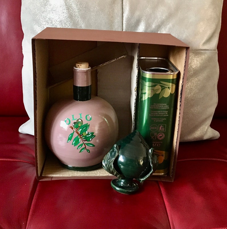 May include: A brown cardboard box with a green ceramic olive oil bottle, a green ceramic olive branch bottle stopper, and a can of olive oil. The can has the text "Olio Extra Vergine di Oliva" and "1 L" printed on it.