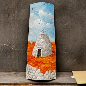 May include: A hand-painted tile depicting a stone building with a white roof against a blue sky with white clouds. The building is surrounded by orange and white stones.