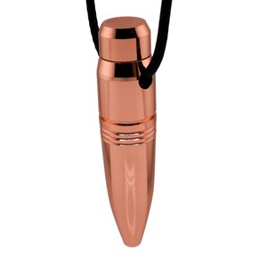Puede incluir: Un collar con un colgante de bala de color cobre y un cordón negro. La bala es lisa y brillante con una parte superior redondeada y una parte inferior puntiaguda.