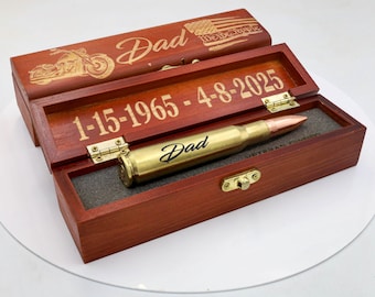 Könnte beinhalten: Eine Holzbox mit Scharnierdeckel, graviert mit dem Wort "Dad" und einem Motorrad. Im Inneren liegt ein messingfarbener, kugelähnlicher Gegenstand auf einem Schaumstoffeinsatz. Die Box zeigt auch die Daten "1-15-1965 - 4-8-2025" und das Wort "Dad" auf der Kugel.