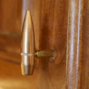 Puede incluir: Una manija de puerta de color dorado en forma de bala con una base de color latón.