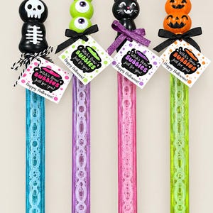 May include: Four Halloween bubble wands with toppers shaped like a skeleton, green monster eyes, a black cat, and orange pumpkins. Each wand features a tag reading Witch's Brew BUBBLES just for you! Happy Halloween! and is tied with a ribbon.