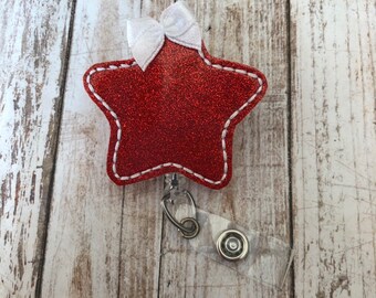 Könnte beinhalten: Roter Glitzer-Stern-Badgehalter mit einer weißen Schleife und einer durchsichtigen, einziehbaren Badge-Rolle.