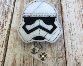 May include: White felt badge holder with a black and white embroidered Stormtrooper design. The badge holder has a clear plastic badge clip with a metal swivel clip.