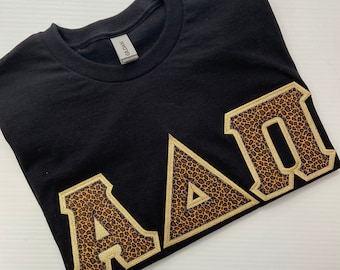 Camiseta negra con letras griegas de hermandad y pequeñas letras con estampado de guepardo.
