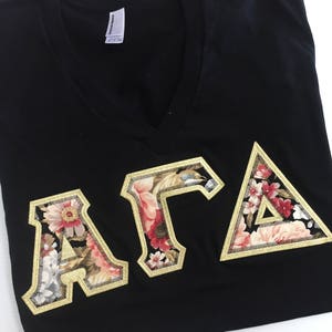 May include: Black v-neck t-shirt with a floral patterned "AFA" embroidered on the front.
