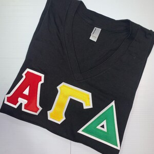 May include: Black v-neck t-shirt with red, yellow, and green Greek letters "AKA" on the front.