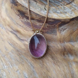 Könnte beinhalten: Eine Halskette mit einem Anhänger aus violettem und weißem Edelstein mit einer goldenen Fassung. Die Halskette liegt auf einer braunen Holzoberfläche.