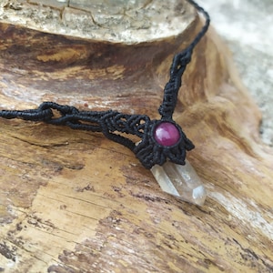 Puede incluir: Un collar de macramé negro con un colgante de cristal de cuarzo transparente y un acento de piedra preciosa rosa.