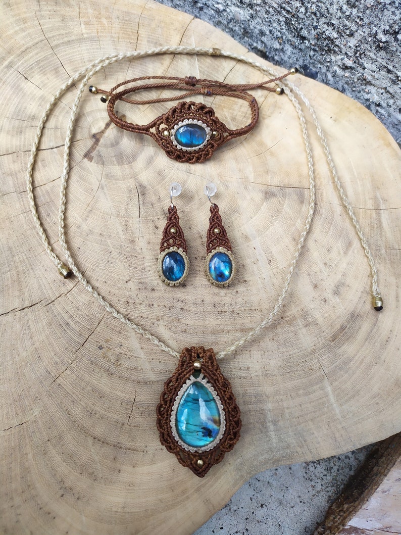 May include: A set of jewelry featuring a brown macrame necklace, bracelet, and earrings with a blue labradorite gemstone pendant.