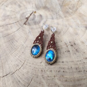 May include: A pair of dangle earrings with blue iridescent stones set in brown macrame with gold accents.