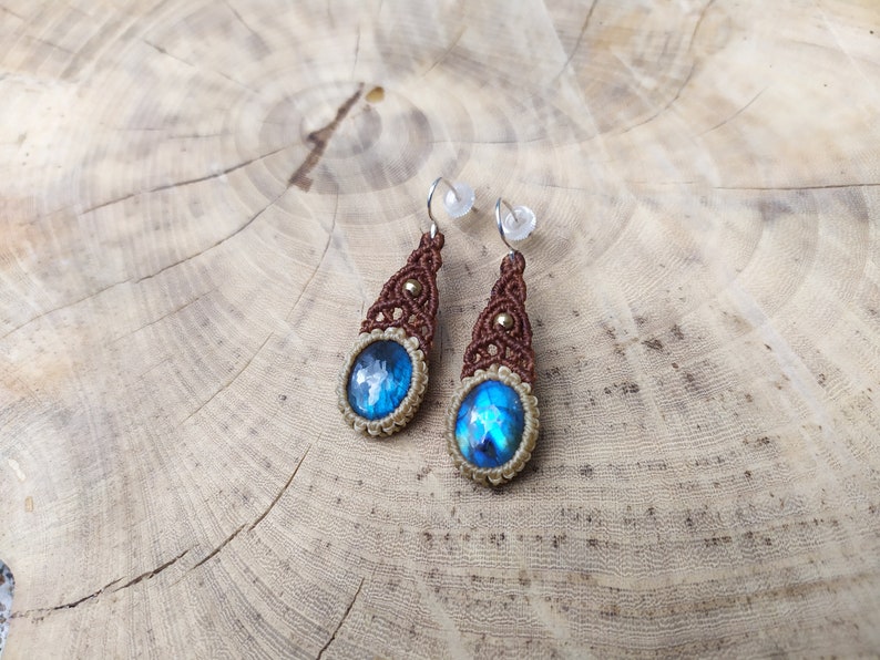 May include: A pair of dangle earrings with blue iridescent stones set in brown macrame with gold accents.