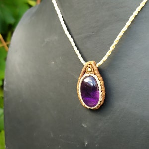 May include: A purple amethyst gemstone pendant necklace with a brown and cream macrame cord.