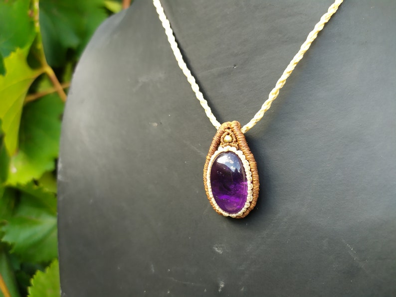May include: A purple amethyst gemstone pendant necklace with a brown and cream macrame cord.