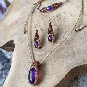May include: A set of amethyst gemstone jewellery featuring a necklace, bracelet, and earrings. The jewellery is made with brown and white cord and gold accents.