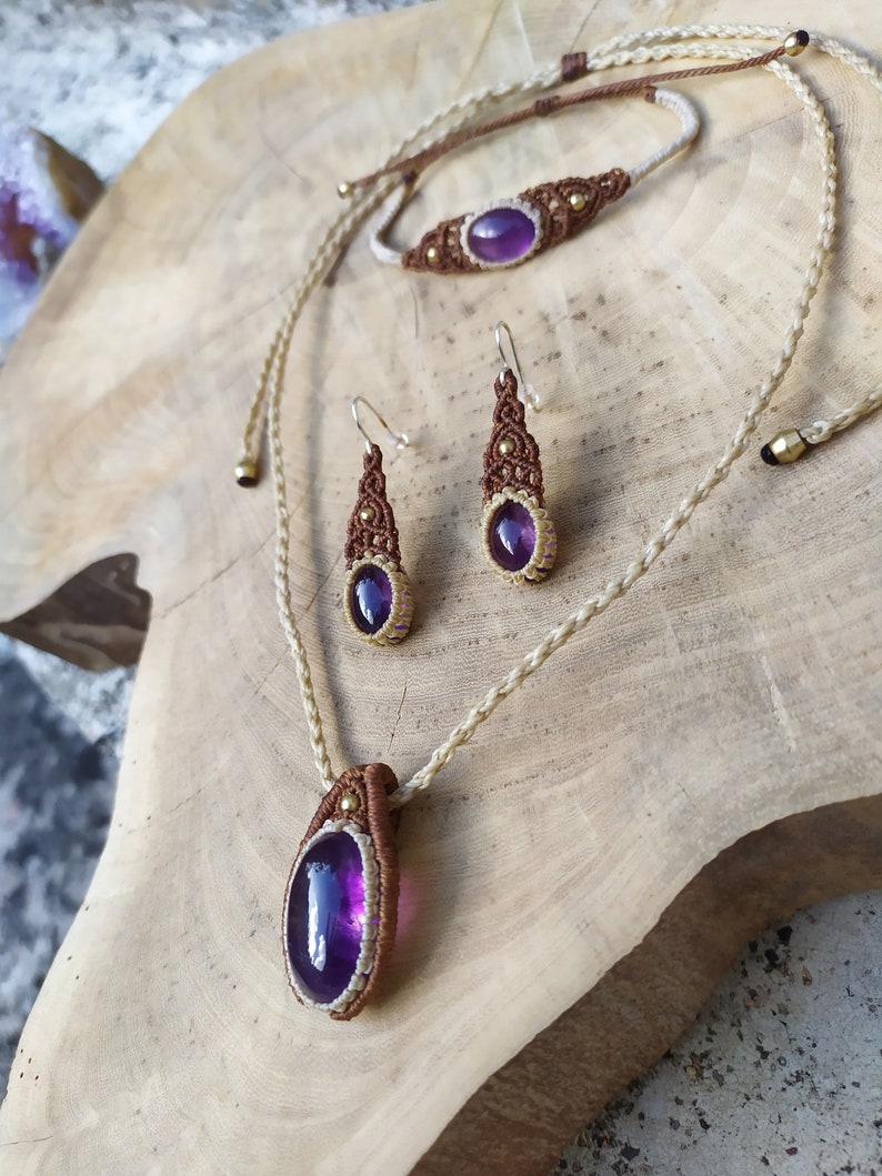 May include: A set of amethyst gemstone jewellery featuring a necklace, bracelet, and earrings. The jewellery is made with brown and white cord and gold accents.