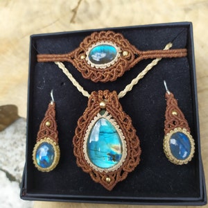 May include: A set of jewelry featuring a brown macrame necklace, bracelet, and earrings with iridescent blue labradorite stones.