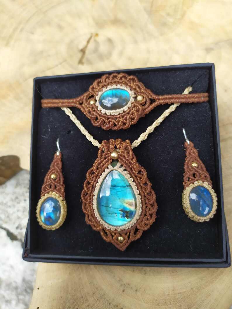 May include: A set of jewelry featuring a brown macrame necklace, bracelet, and earrings with iridescent blue labradorite stones.