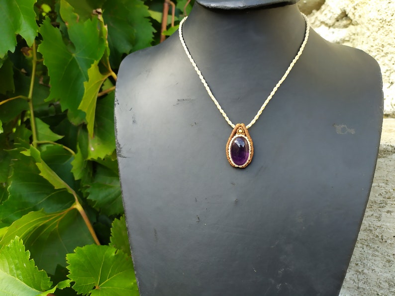 May include: A purple amethyst gemstone pendant necklace with a brown leather cord and a white macrame cord.