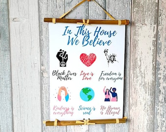 May include: A white canvas scroll with the text "In This House We Believe" and various illustrations and text, including "Black Lives Matter", "Love is Love", "Freedom is for everyone", "Kindness is everything", "Science is real", and "No Human is Illegal".