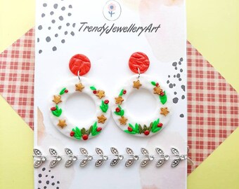 May include: A pair of white and green Christmas wreath earrings with red berries and gold stars. The earrings are on a white card with the text "TrendyJewelleryArt".