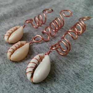May include: Three copper wire hair coils with white cowrie shells attached. The coils are designed to hold hair in place.