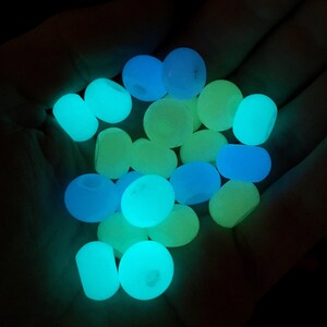 May include: A collection of glow-in-the-dark marbles in shades of blue, green, and yellow. The marbles are smooth and round, and they are arranged in a pile.