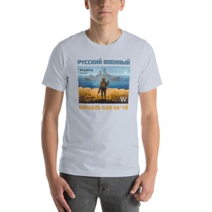 May include: Light blue t-shirt featuring a stamp design with a soldier, ship, and text in Russian and Ukrainian. The stamp design includes the text "Russian Military", "Ukraine", and "2022".