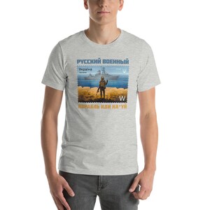 May include: A light gray t-shirt featuring a postage stamp design with a soldier, ship, and text in Russian and Ukrainian. The stamp design includes the year 2022 and the letter "W".