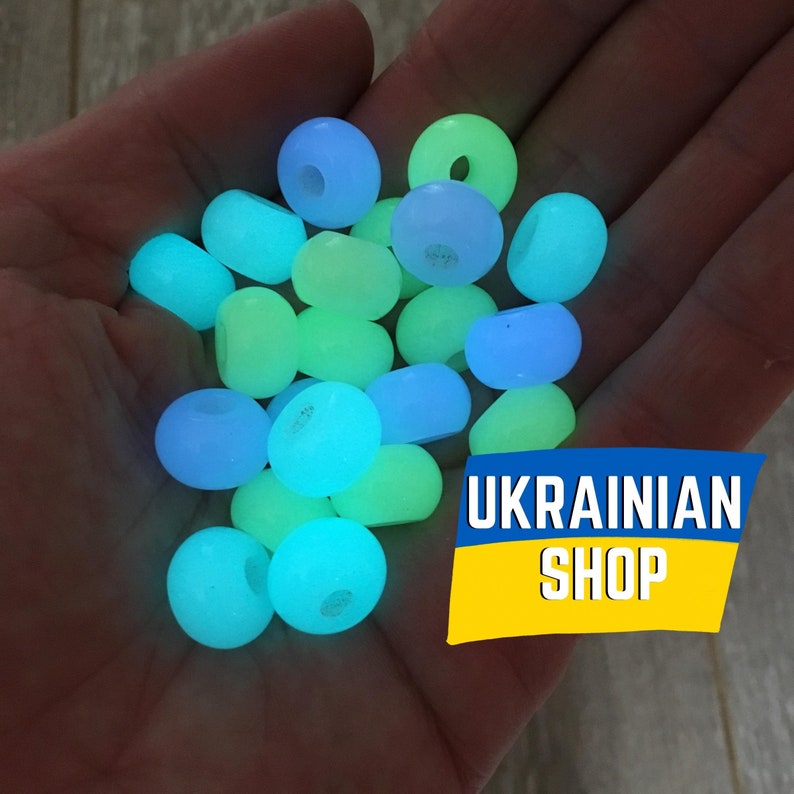 May include: A hand holding a collection of glow-in-the-dark beads in shades of blue and green. The beads are round and have a smooth, glossy finish. The text "UKRAINIAN SHOP" is visible in the lower right corner of the image.