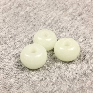 May include: Three white glow-in-the-dark beads with a hole in the center. The beads are on a gray fabric background.