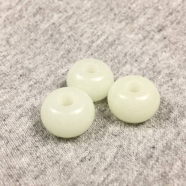 May include: Three white glow-in-the-dark beads with a hole in the center. The beads are on a gray fabric background.