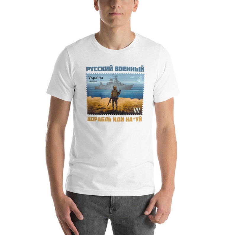 May include: White t-shirt featuring a stamp design with a soldier, a warship, and text in Cyrillic script. The stamp design includes the text "RUSSIAN MILITARY" and "UKRAINE". The shirt also has the text "SHIP GO F*** YOU".