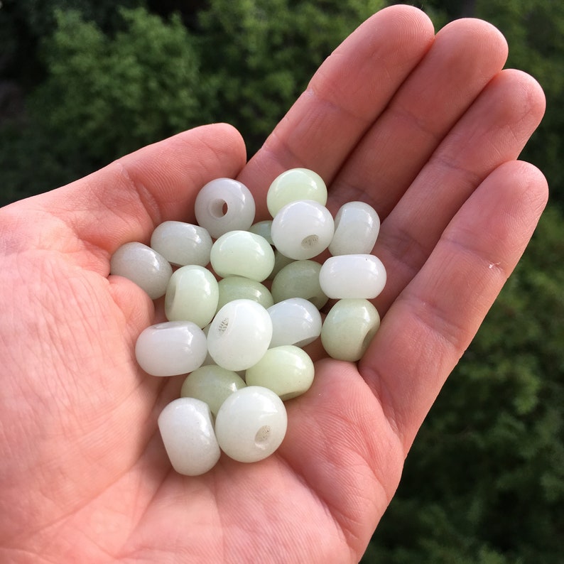 May include: A pile of smooth, white beads with a hole in the center. The beads are translucent and have a slight green tint.