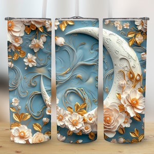 May include: A tall, insulated tumbler with a celestial design. The light blue background features a crescent moon and floral accents in white and gold. The flowers and moon appear to be 3D, adding depth to the design. Includes a straw and lid.