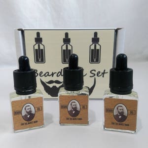 May include: Three small glass bottles with dropper tops, each containing beard oil. The bottles have brown labels with the words "Beard Oil" and "For the Manly Man" printed on them. The bottles are arranged in a row on a white surface.