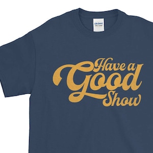 May include: A navy blue t-shirt with a yellow retro-style graphic that says "Have a Good Show".