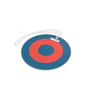 May include: A round luggage tag with a blue background and a red bullseye design. The tag has a white string for attachment. The design is simple and modern, suitable for travel.