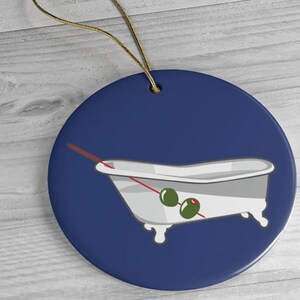 May include: A blue and white ceramic ornament with a white bathtub filled with green olives and a red stick. The ornament is shaped like a circle.