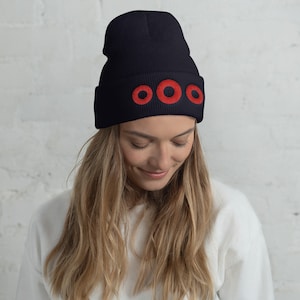 Puede incluir: Un gorro azul marino con tres círculos rojos bordados en la parte delantera. El gorro está hecho de un material suave y tejido y está diseñado para ser usado en la cabeza. Este gorro de invierno es un accesorio elegante.