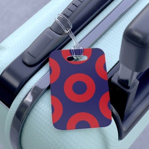 May include: A blue luggage tag with a red and white donut pattern. The tag has a hole at the top for attaching to luggage.