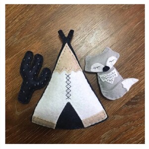 K&ouml;nnte beinhalten: Filz-Applikationsset mit einem Tipi, einem Kaktus und einem schlafenden Fuchs. Das Tipi ist wei&szlig; mit schwarzen und braunen Akzenten. Der Kaktus ist schwarz mit wei&szlig;en N&auml;hten. Der Fuchs ist grau mit schwarzen Augen und einem wei&szlig;en Schwanz.