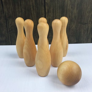 May include: A set of wooden bowling pins and a ball, all in a natural wood color. The pins are arranged in a triangle formation, with the ball in front of them.
