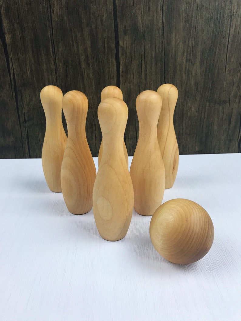 May include: A set of wooden bowling pins and a ball, all in a natural wood color. The pins are arranged in a triangle formation, with the ball in front of them.