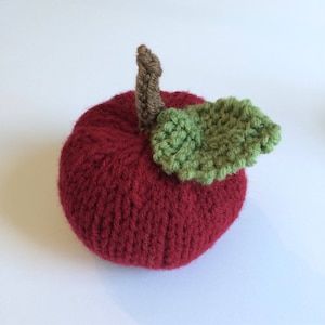 May include: A knitted red apple with a green leaf and a brown stem.